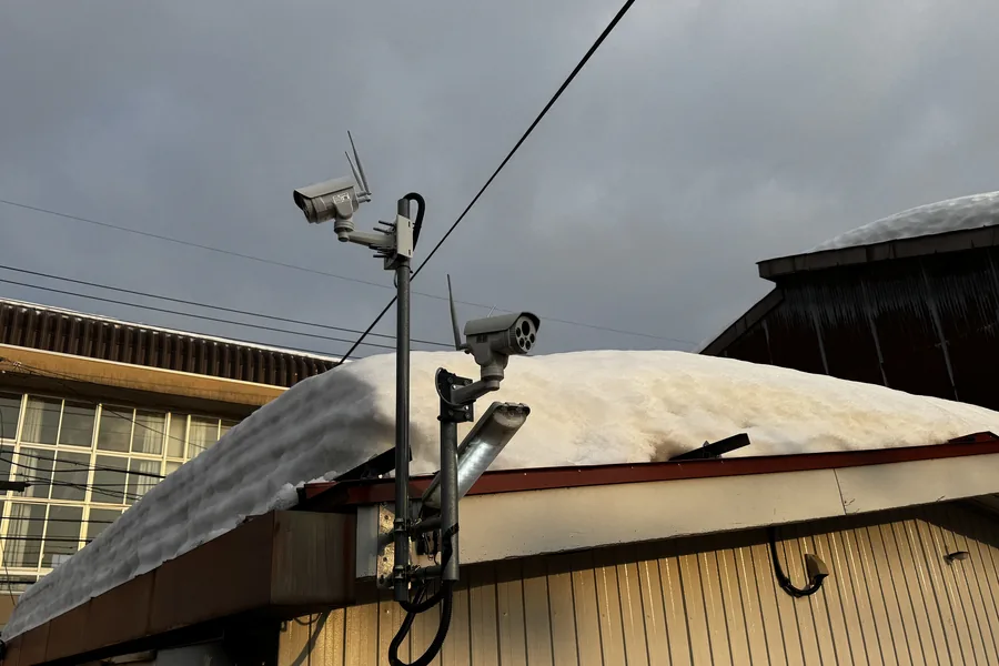 積雪した建物の軒先にポールを立てて設置したワイヤレス防犯カメラ2台